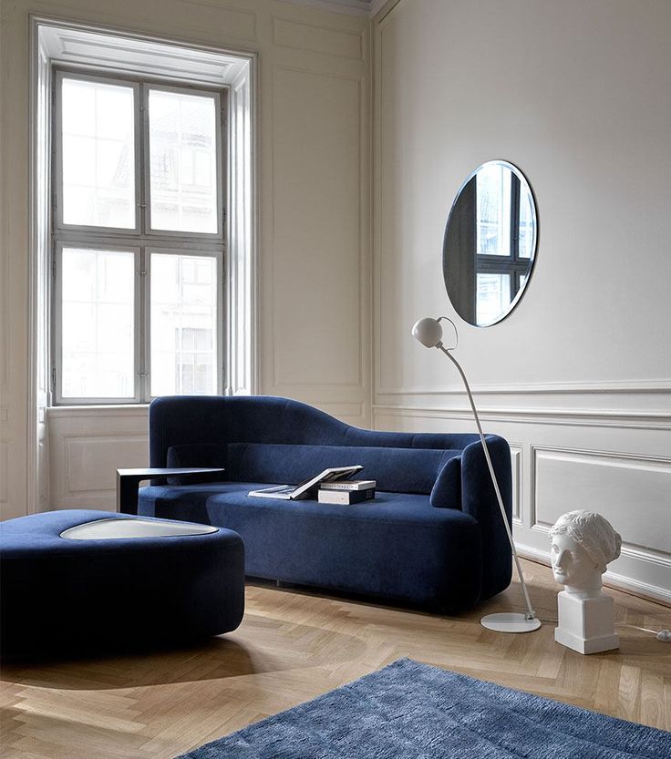Modern living room with navy sofa, round mirror, floor lamp, and stylish decor in a bright, elegant space.