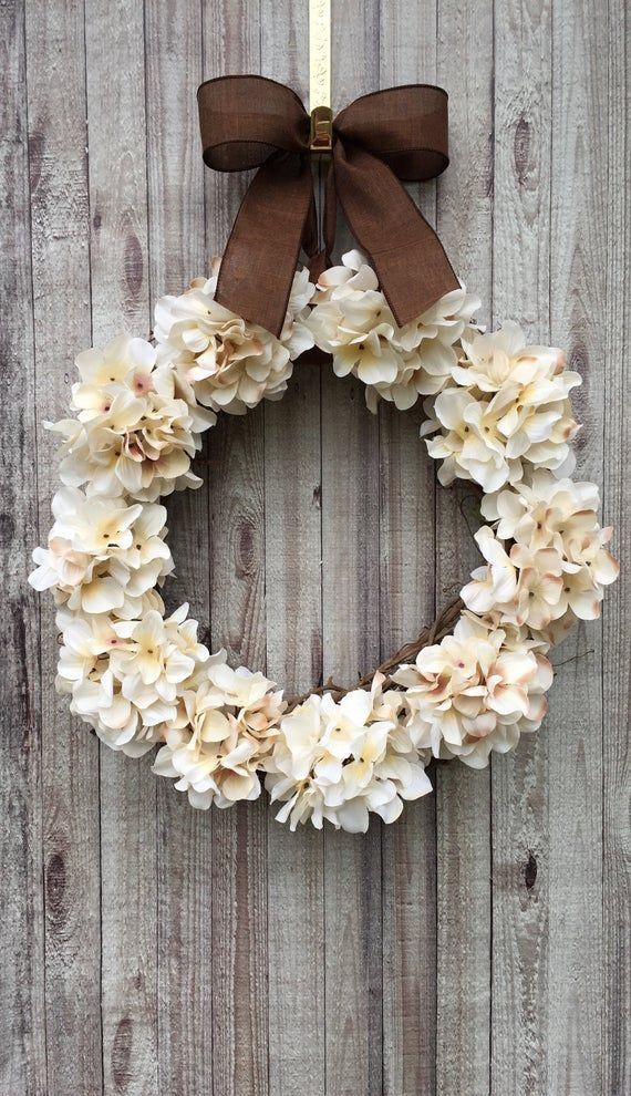 Cream hydrangea wreath with a brown bow on rustic wood background. Perfect for elegant home decor or seasonal display.