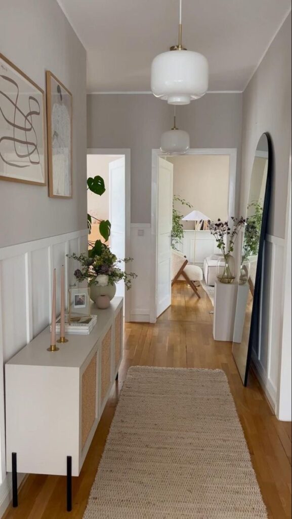 Modern hallway with wooden flooring, stylish furniture, and decor, leading to a bright living room with plants and art.