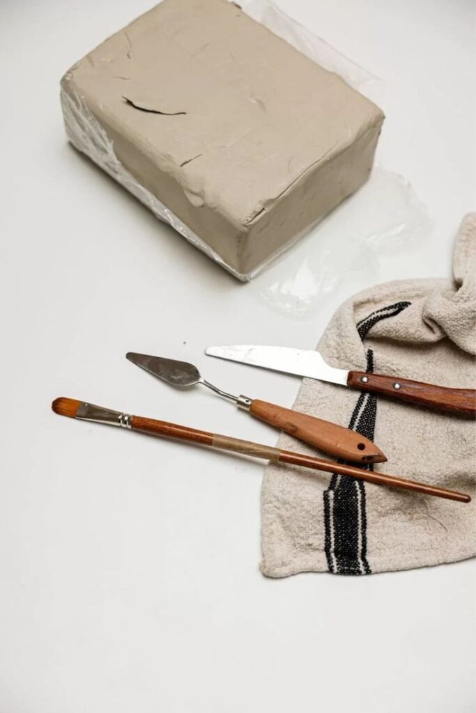 Clay block with sculpting tools and cloth on white background, ideal for pottery or crafting projects.
