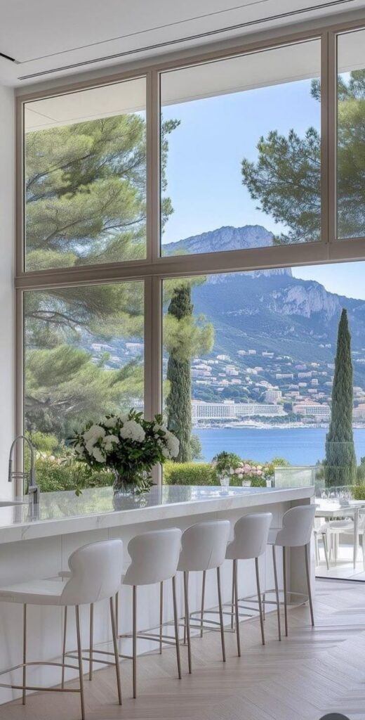 Modern kitchen with panoramic windows, overlooking a serene coastal landscape and distant mountains.