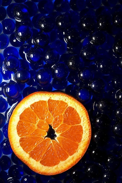 Orange slice on glossy blue glass pebbles background, creating a vibrant contrast and fresh aesthetic.