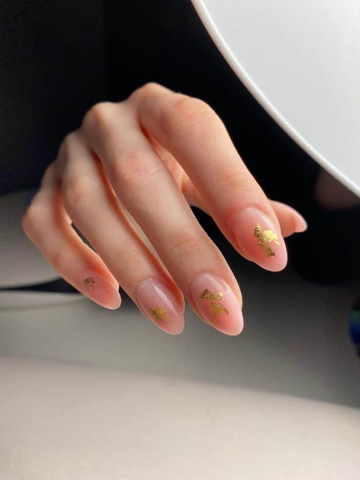 Elegant hand with almond-shaped nails adorned with gold leaf design under soft lighting.