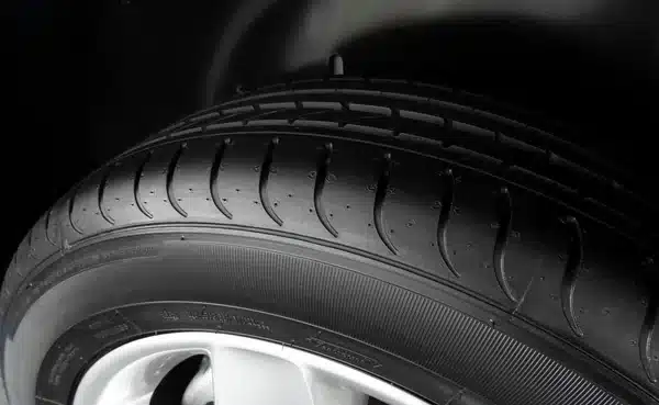 Close-up of a black car tire with detailed tread pattern, mounted on a silver rim for enhanced vehicle grip and performance.