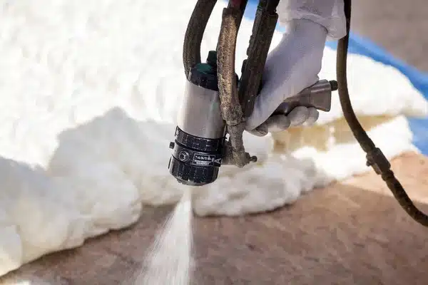 Worker applies spray foam insulation on wall for energy efficiency and thermal protection in construction project.