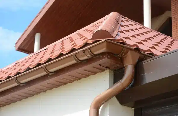 Red-tiled roof with brown gutters and downspouts on a residential home under a clear blue sky.