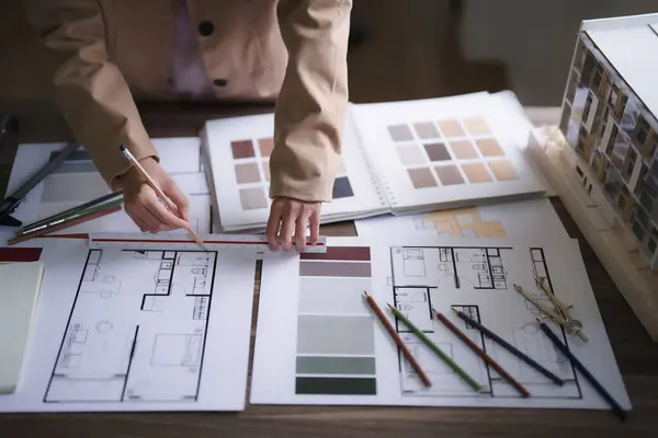 Interior designer reviewing floor plans and color swatches on a desk, surrounded by pencils and architectural models.