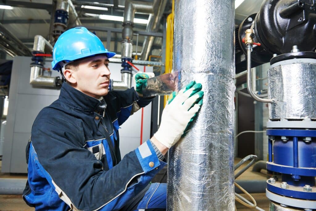 download 4 Industrial worker insulating pipes with foil in a mechanical room, wearing safety helmet and gloves. | Sky Rye Design Industrial worker insulating pipes with foil in a mechanical room, wearing safety helmet and gloves.