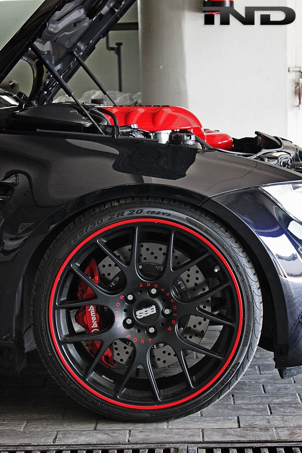 Close-up of a sporty car wheel with red accents, showcasing a red engine and Brembo brake inside.