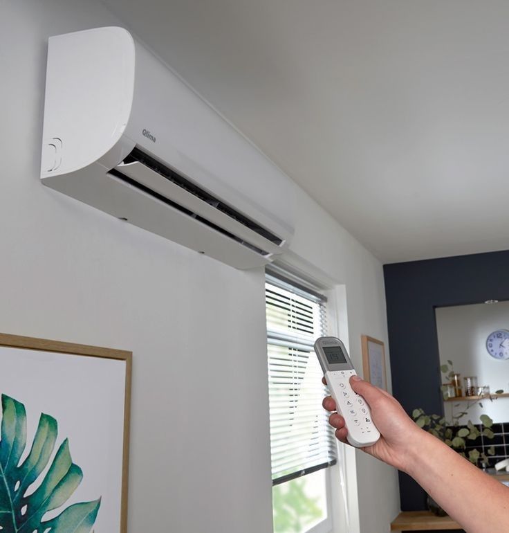 Person using remote to control wall-mounted air conditioner in modern living room.