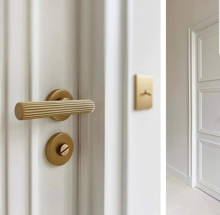 Elegant brushed gold door handle on white panel door in a modern interior setting.