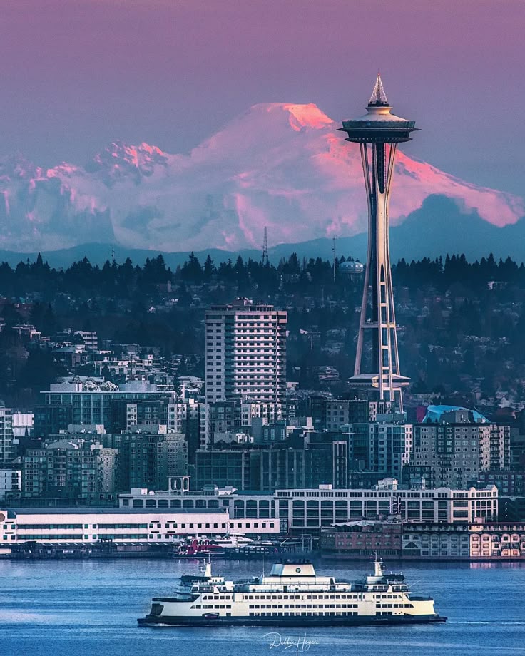 Seattle skyline at sunset featuring the Space Needle with majestic mountains in the background and a ferry in the foreground.