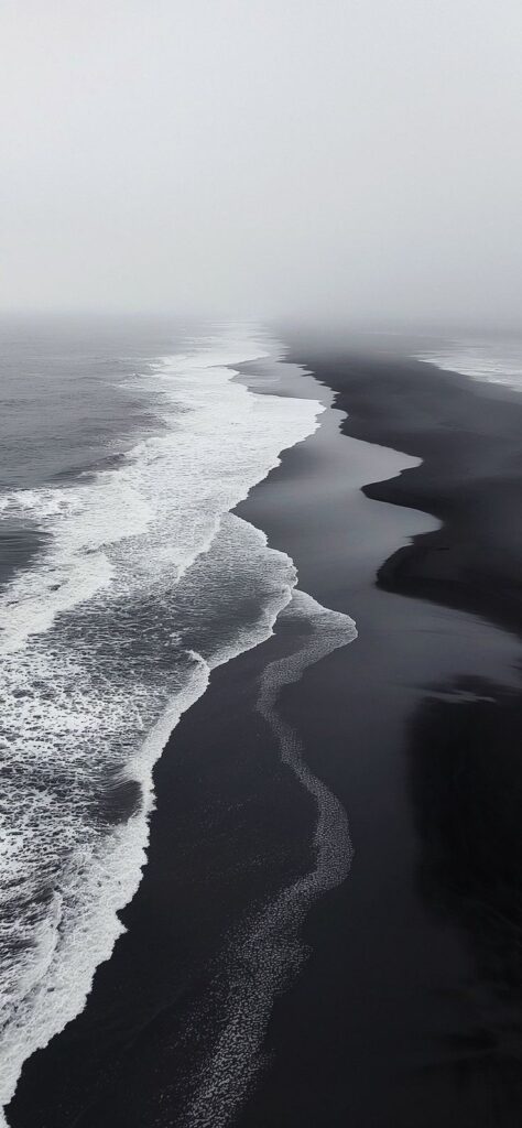Misty black sand beach with gentle waves and cloudy skies.