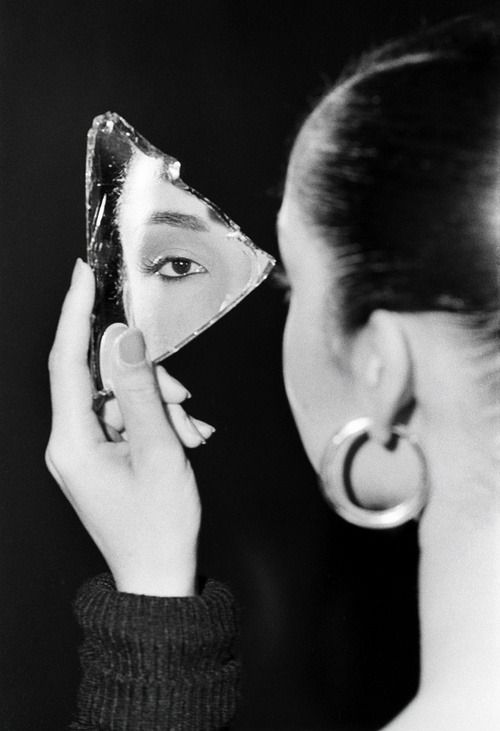 Woman's eye reflected in triangular glass shard, close-up shot with focus on detail and mystery.