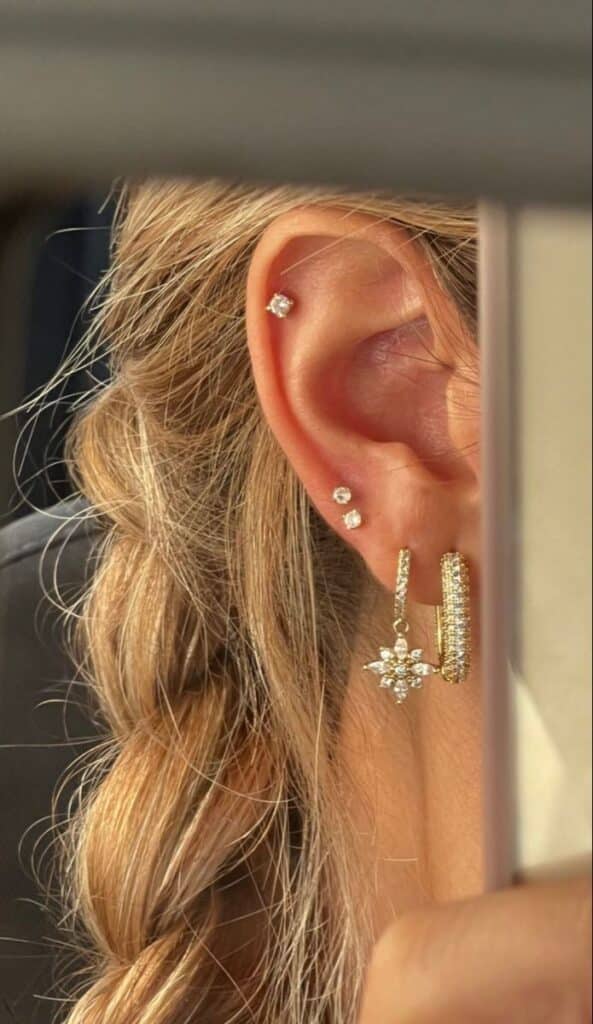 Close-up of an ear adorned with elegant gold earrings and piercings, featuring diamonds and a star-shaped design.