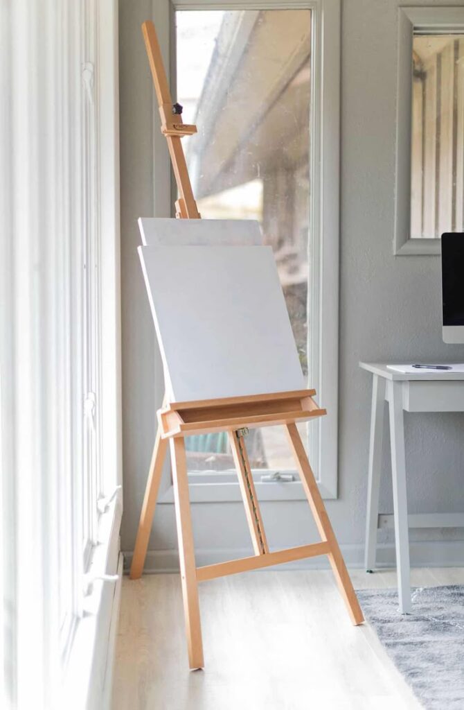 Wooden easel with blank canvas by bright windows in modern art studio.
