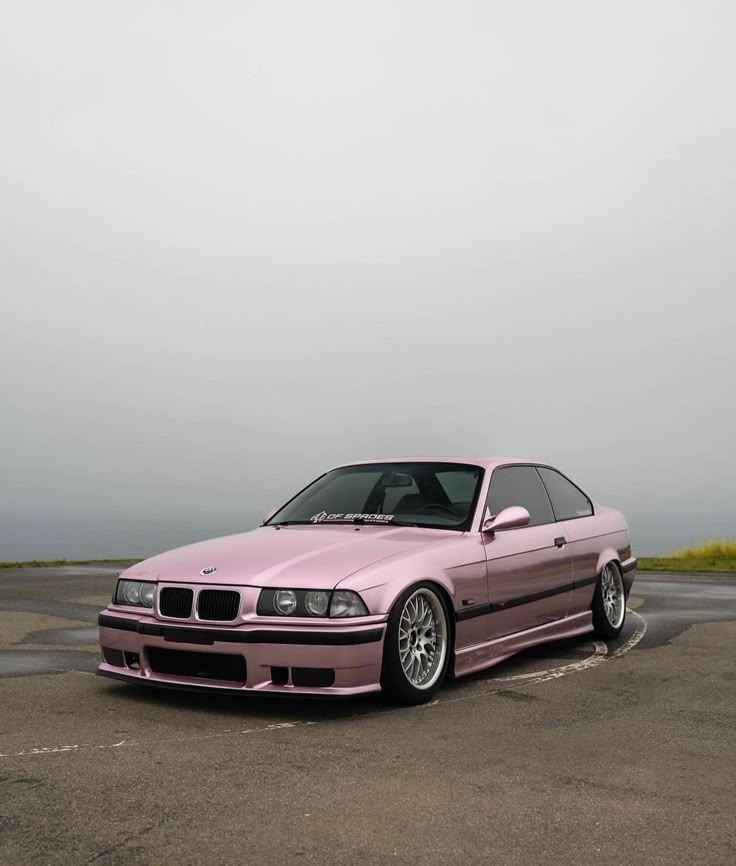 Pink vintage BMW coupe parked on a cloudy day, showcasing stylish rims and a sleek body design.