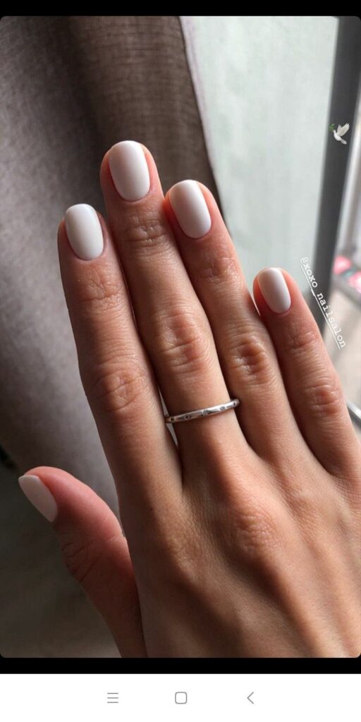 White matte manicure with a silver ring on a hand, showcasing elegant and minimalist nail design.