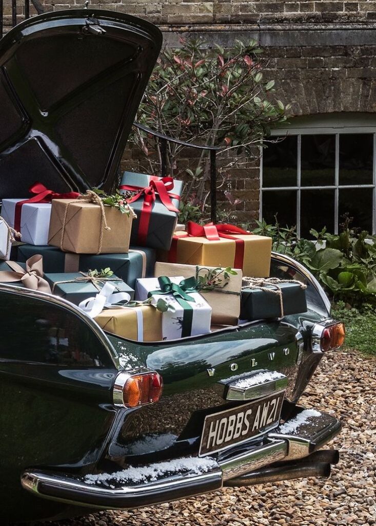 Vintage car trunk filled with wrapped holiday gifts, set in a garden.