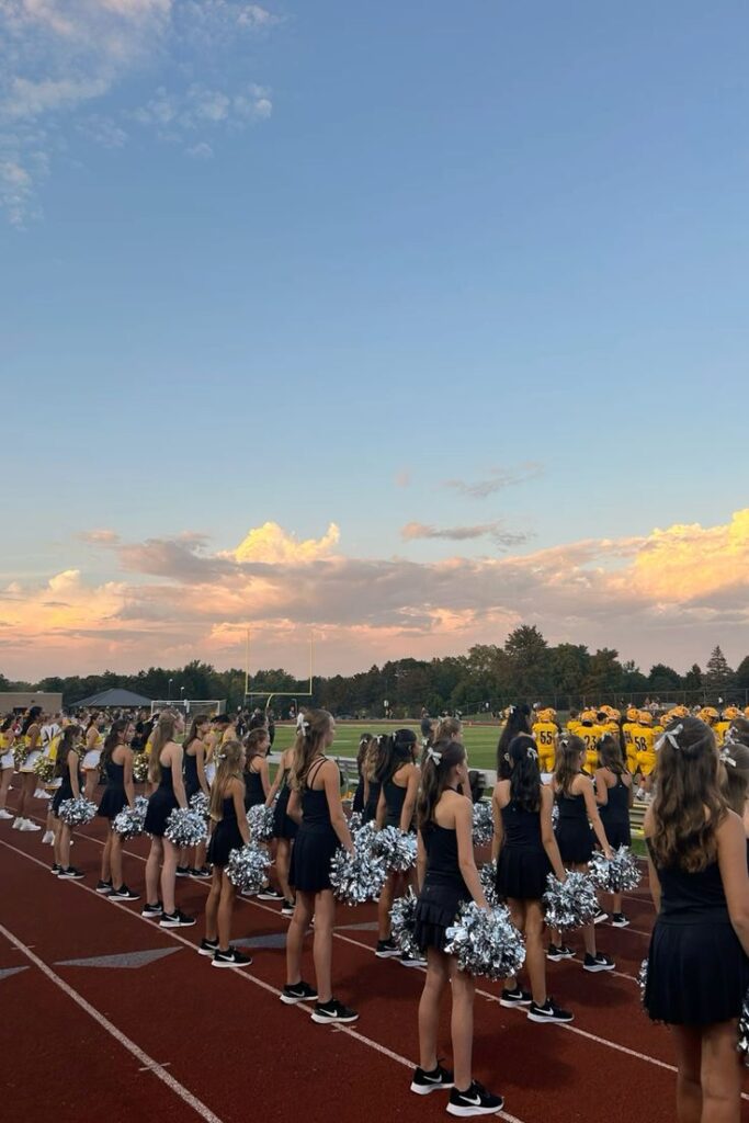 Cheerleaders in formation on a football field at sunset, ready to support their team in matching uniforms.