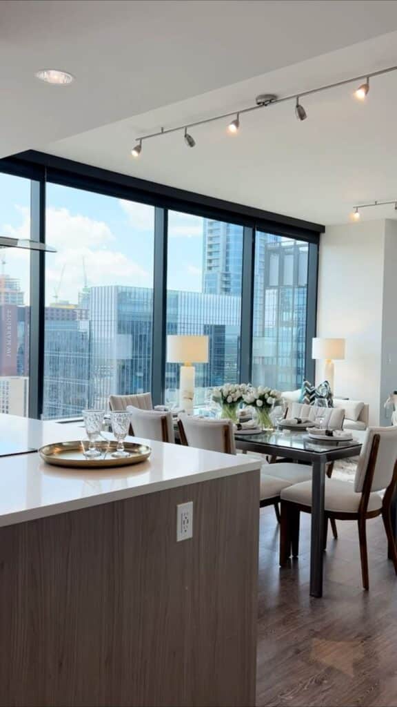 Modern dining area with city view, featuring elegant table setting and floor-to-ceiling windows in a high-rise apartment.