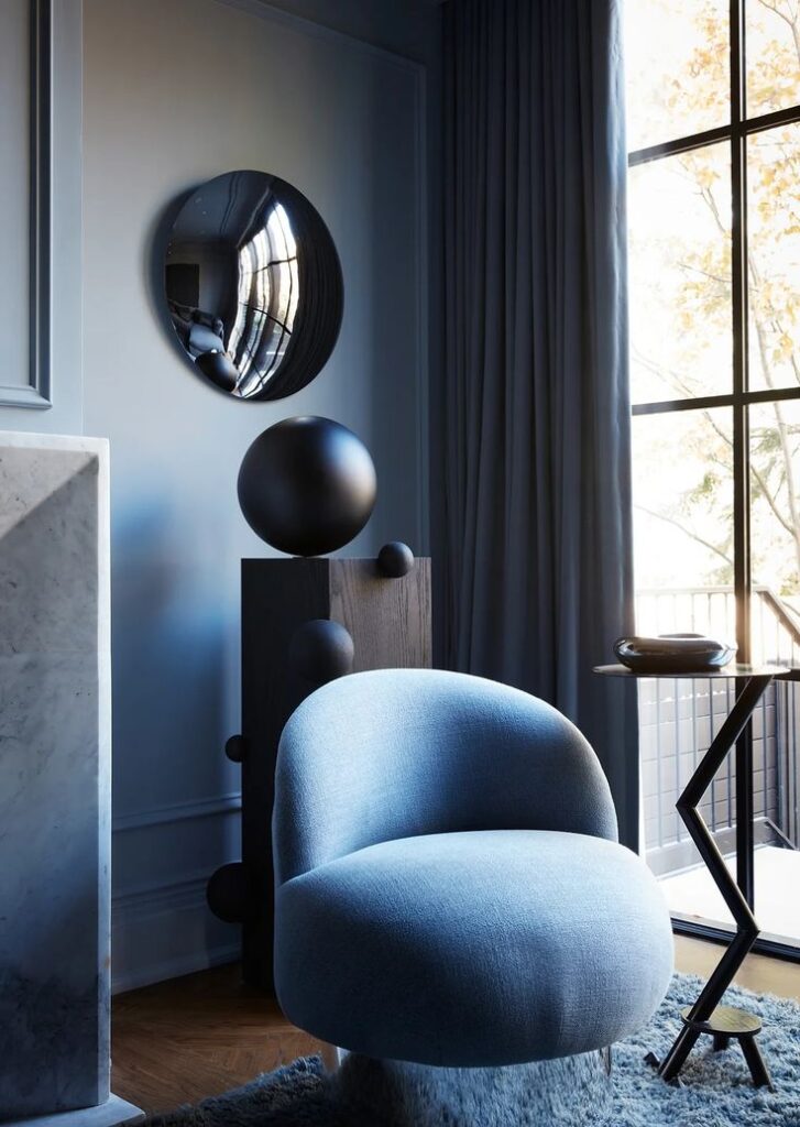 Modern living room with blue chair, abstract art, round mirror, and tall windows. Sleek interior design aesthetic.