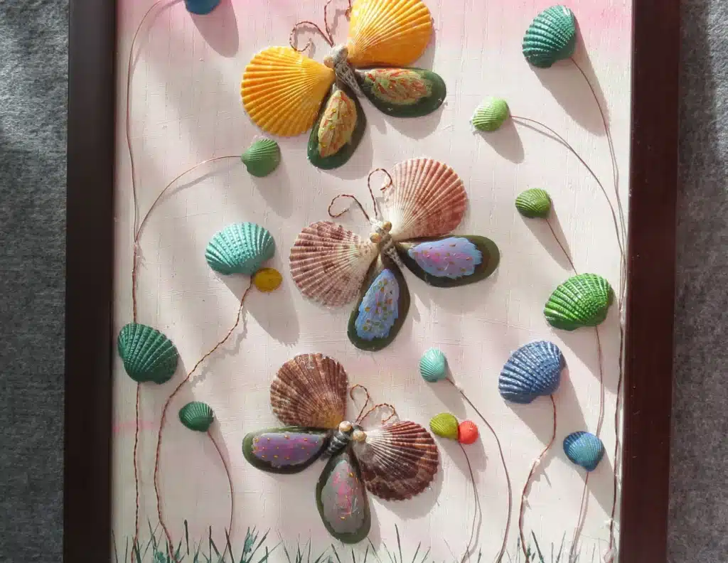 Creative butterfly artwork using colorful seashells framed on a textured background.