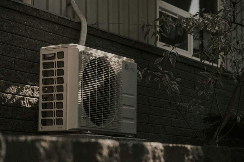 image Outdoor air conditioning unit mounted on a brick wall outside a house, surrounded by greenery. | Sky Rye Design Outdoor air conditioning unit mounted on a brick wall outside a house, surrounded by greenery.