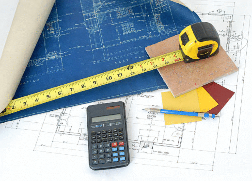 Various architectural tools on blueprints: calculator, tape measure, pen, color samples, and tile.