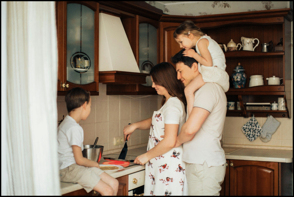 image Family cooking together in a cozy kitchen, mom making pancakes, dad with daughter on shoulders, son perched on counter. | Sky Rye Design Family cooking together in a cozy kitchen, mom making pancakes, dad with daughter on shoulders, son perched on counter.