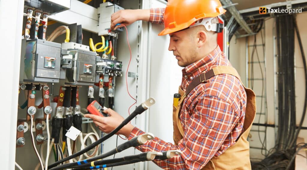 Electrician in hard hat checking electrical panel with multimeter.