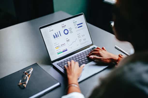 Person analyzing data on a laptop with charts and graphs in an office setting.