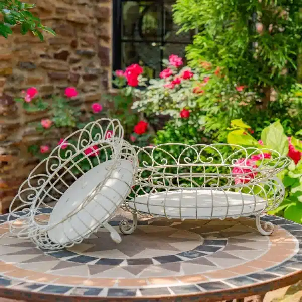 Ornate metal baskets on a mosaic table in a blossoming garden, showcasing vibrant flowers and lush greenery.