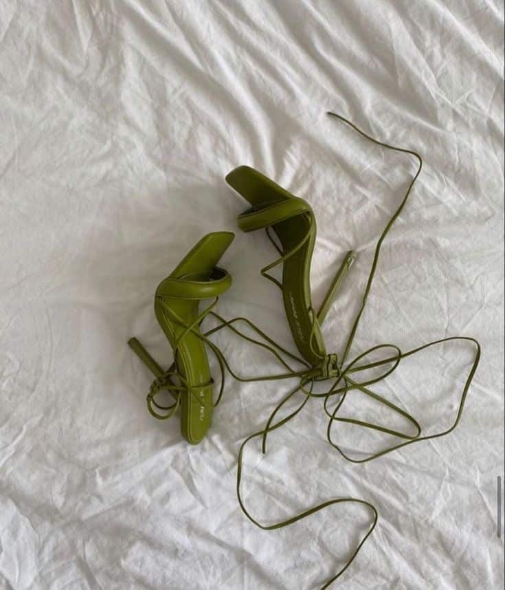 Olive green strappy high heels with long laces on white fabric, showcasing elegant fashion footwear.