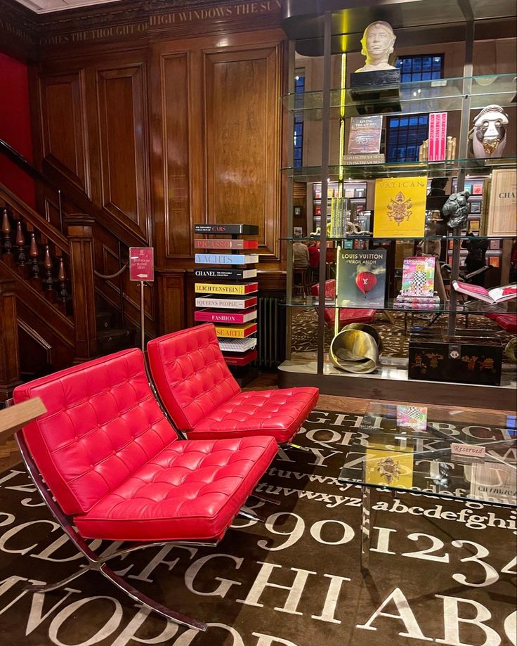 Cozy library corner with red chairs, wooden panels, art books, and eclectic decor on a patterned carpet.
