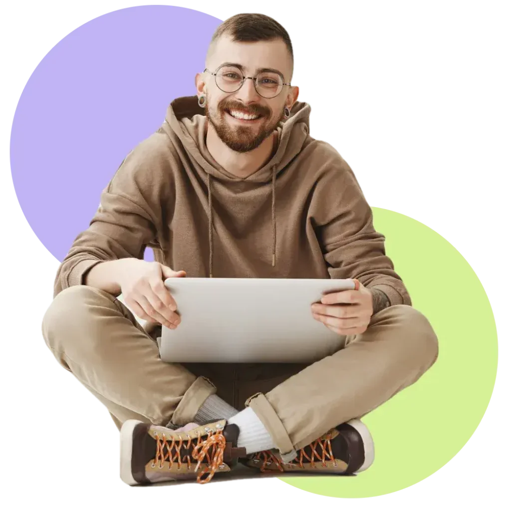 Smiling person in casual wear using a tablet, sitting cross-legged against a colorful background.