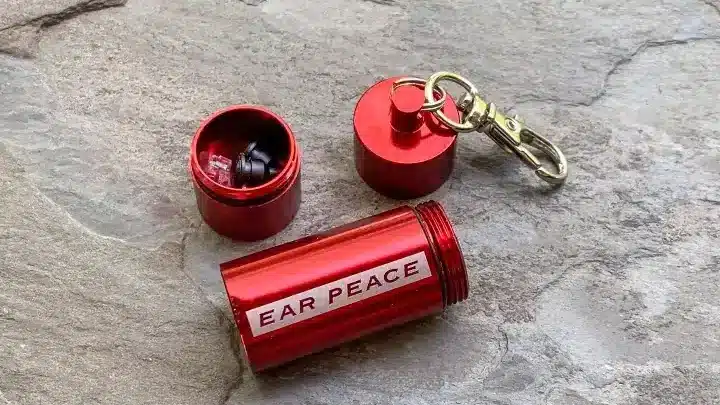 Red EarPeace earplugs case with keychain, open on stone background, showcasing reusable ear protection.