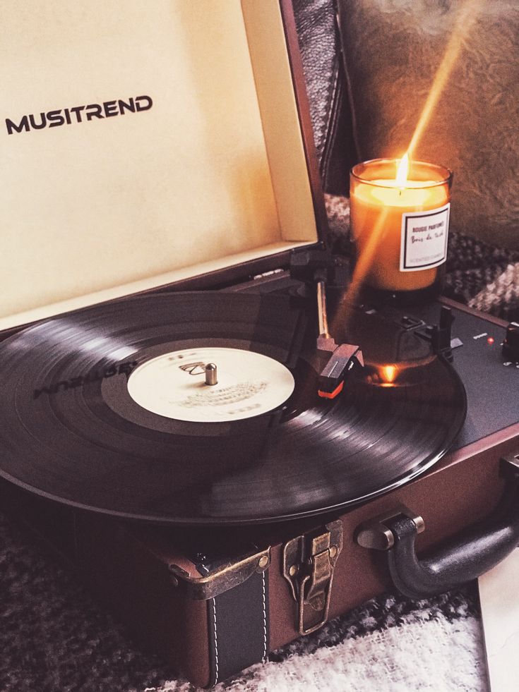 Vintage record player with spinning vinyl beside a lit candle, creating a cozy and nostalgic ambiance.