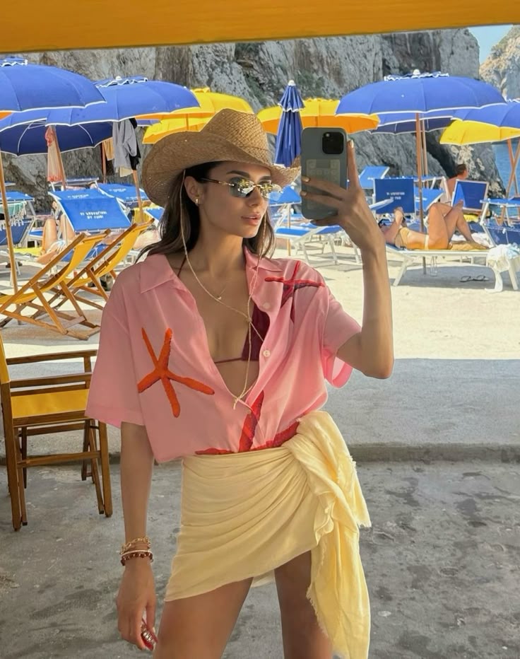 Woman in beachwear takes a selfie at beach with colorful umbrellas and lounge chairs.