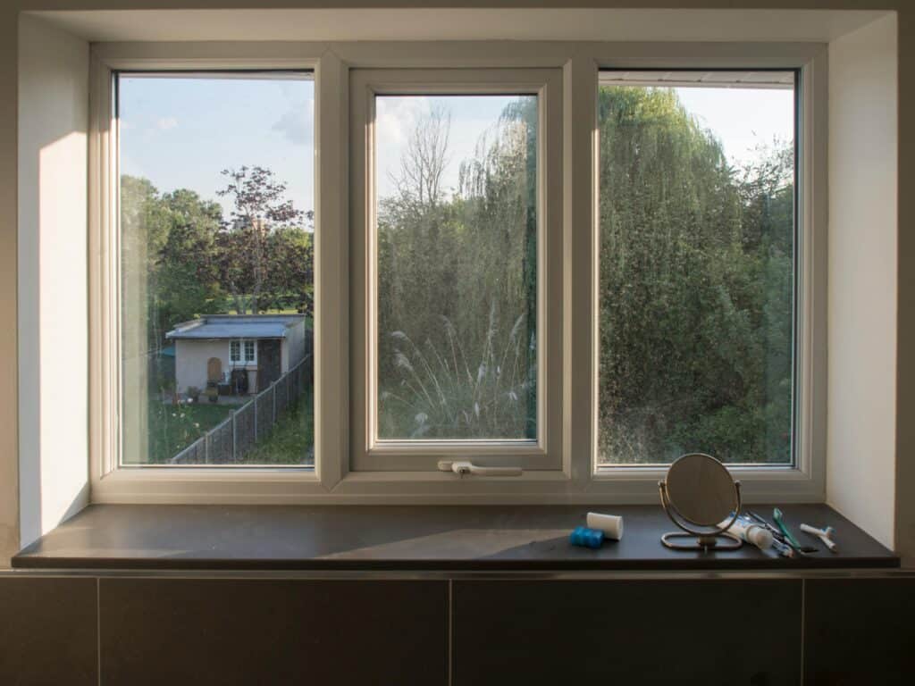 View from a window overlooking a garden with trees and a small shed, with bathroom items on the windowsill.