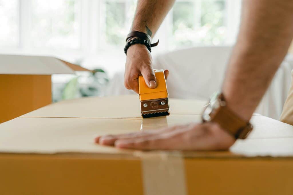 pexels-ketut-subiyanto-4246095 Person sealing a cardboard box with tape in a bright room, emphasizing packing and shipping activities. | Sky Rye Design Person sealing a cardboard box with tape in a bright room, emphasizing packing and shipping activities.