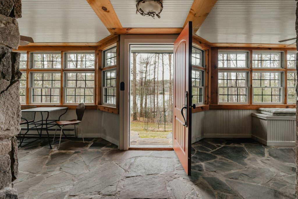 photo-1713365777421-8cb731049c18 Rustic room with open door to forest view, stone floor, wooden trim, and cozy seating. | Sky Rye Design Rustic room with open door to forest view, stone floor, wooden trim, and cozy seating.