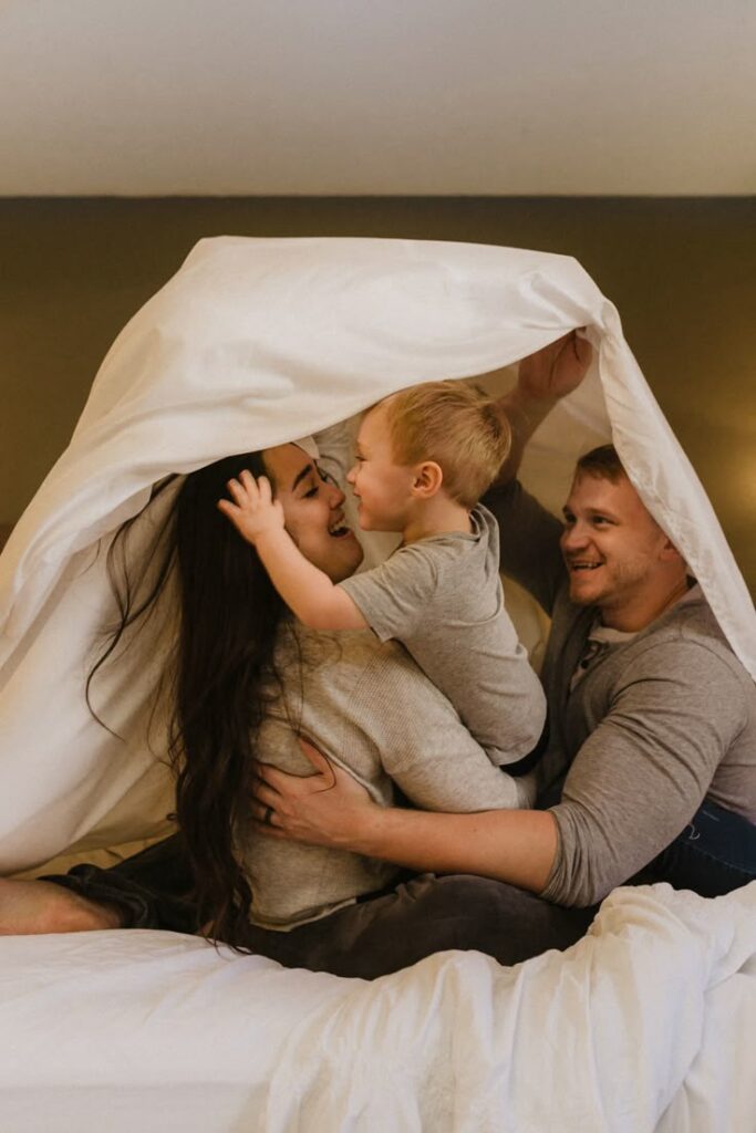 Family playing in bed under sheets, smiling and bonded, creating happy memories together.