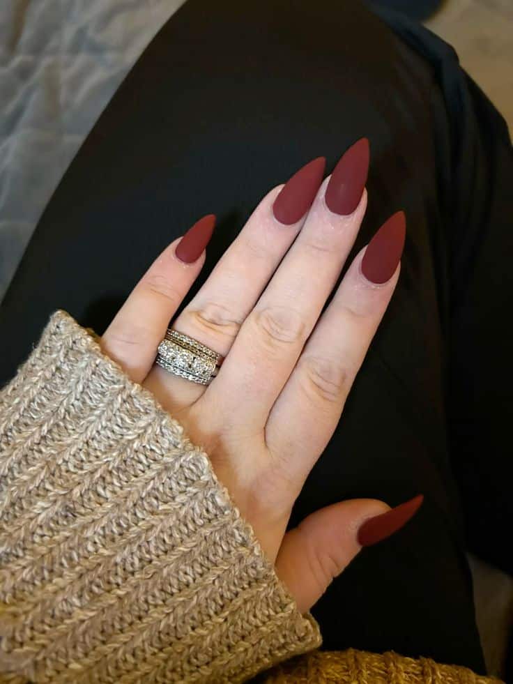 Maroon stiletto nails with silver rings, cozy knit sweater, black leggings. Stylish nail art and chic accessories.