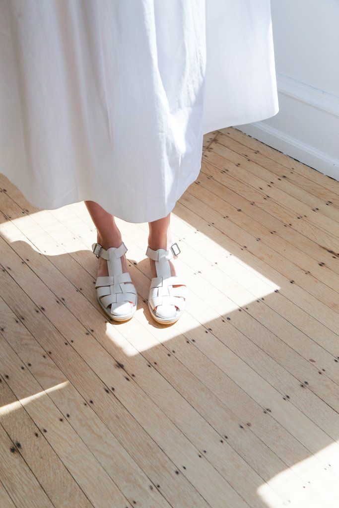 White dress and woven sandals on light wooden floor in bright sunlight.