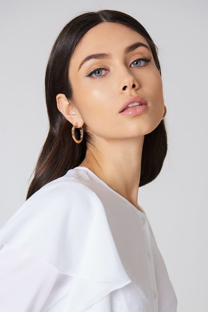 rose calloway cobalt Fashionable woman with long dark hair, wearing gold hoop earrings and a white blouse, looking confidently at the camera. | Sky Rye Design Fashionable woman with long dark hair, wearing gold hoop earrings and a white blouse, looking confidently at the camera.