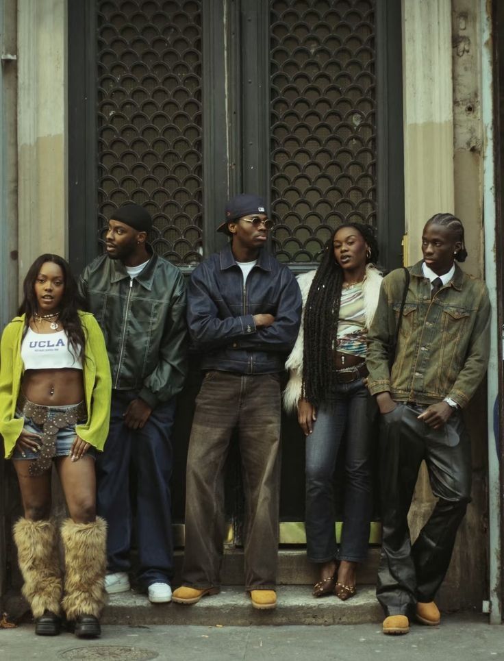 Group of stylish young adults in casual urban outfits standing against a wall, showcasing diverse fashion trends.