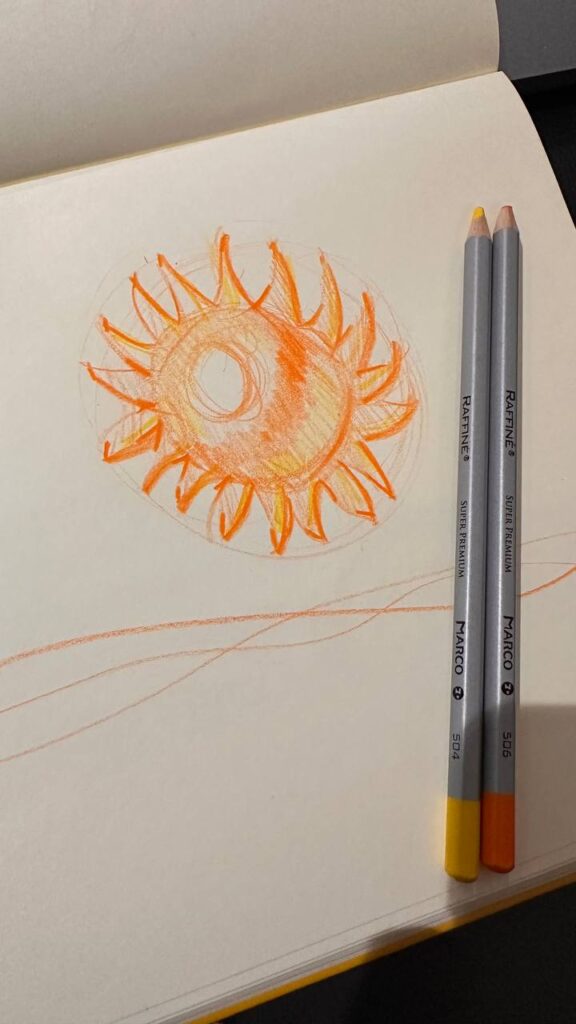 Orange sun sketch in sketchbook with yellow and orange colored pencils on page