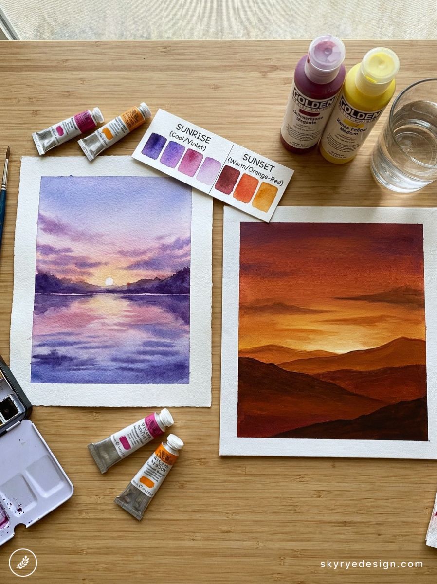 Two watercolor landscape paintings on white textured paper—left shows a purple sunrise over water, right shows an orange sunset over rolling hills, with paints and swatches on a wooden table.