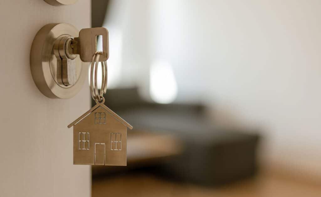 Key in door with house-shaped keychain, symbolizing home ownership and real estate investing.
